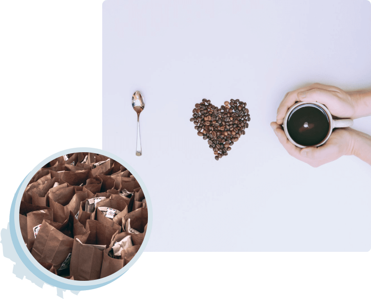 A white surface with a silver spoon, a heart made of coffee beans, and hands holding a coffee cup.