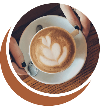 Hands hold a white mug with a latte and a heart design in the foam, on a white plate with a spoon.