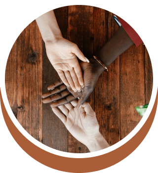 Three hands with varying skin tones are stacked on a wooden surface, palms open.