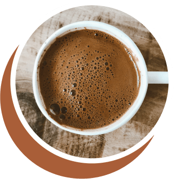 A cup of black coffee with a foamy top, seen from above, on a wooden surface.
