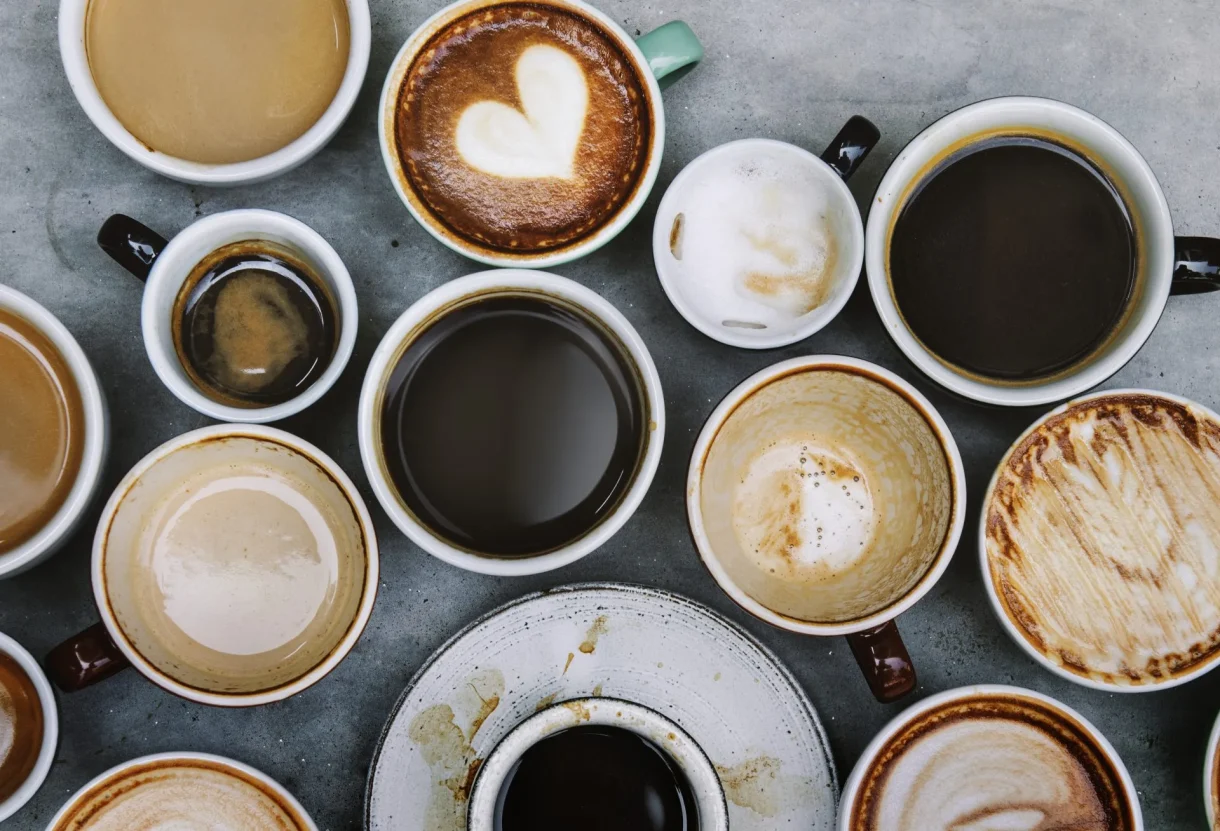 Multiple empty and partially empty coffee cups with stains and foam residue scattered on a gray marble surface.