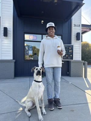 Jalen Coker standing outside Canal Coffee with a large dog next to him and a pup cup in his hand.
