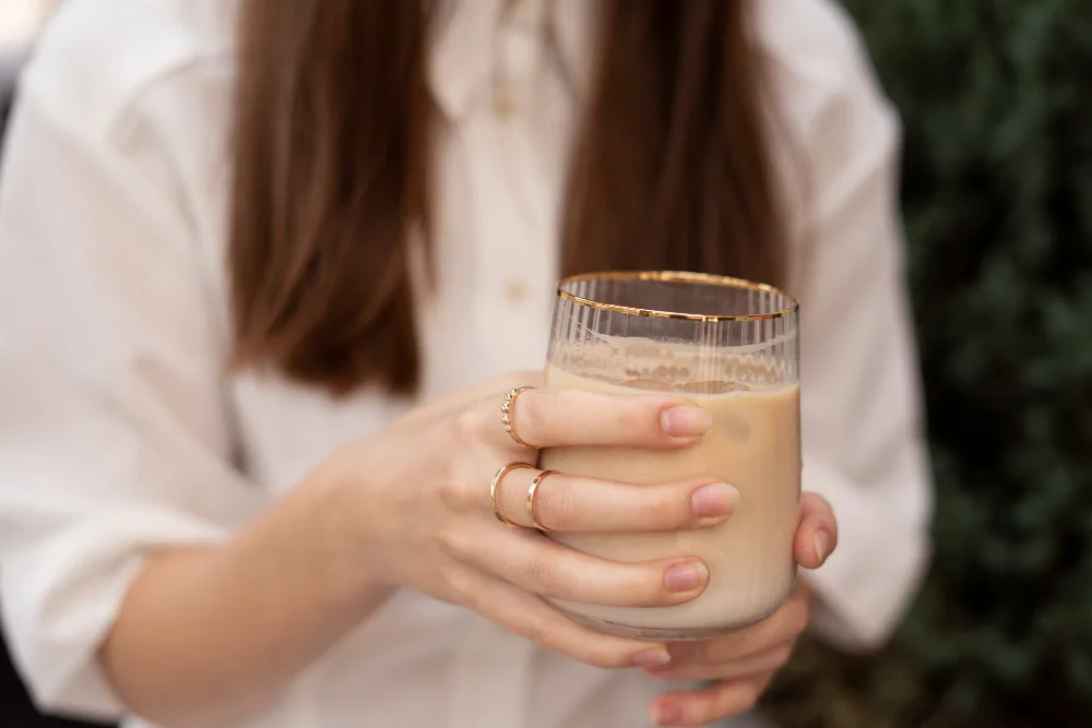 Person holding a creamy iced coffee in a clear glass.