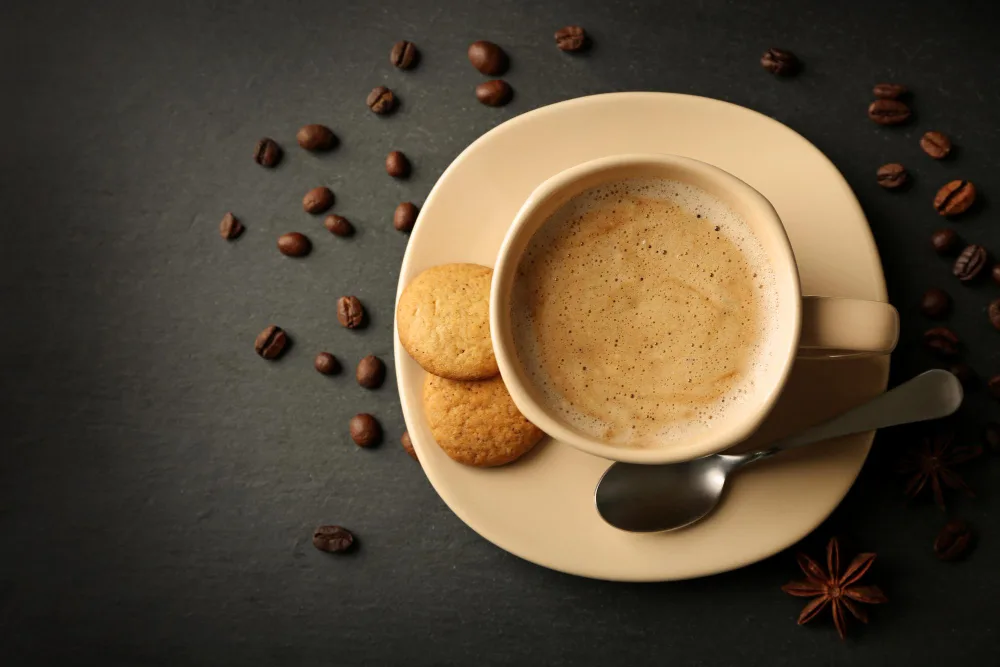 Cup of coffee with cookies, spoon, coffee beans, and star anise.