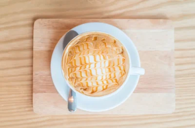 Cup of caramel latte with latte art on a wooden tray.