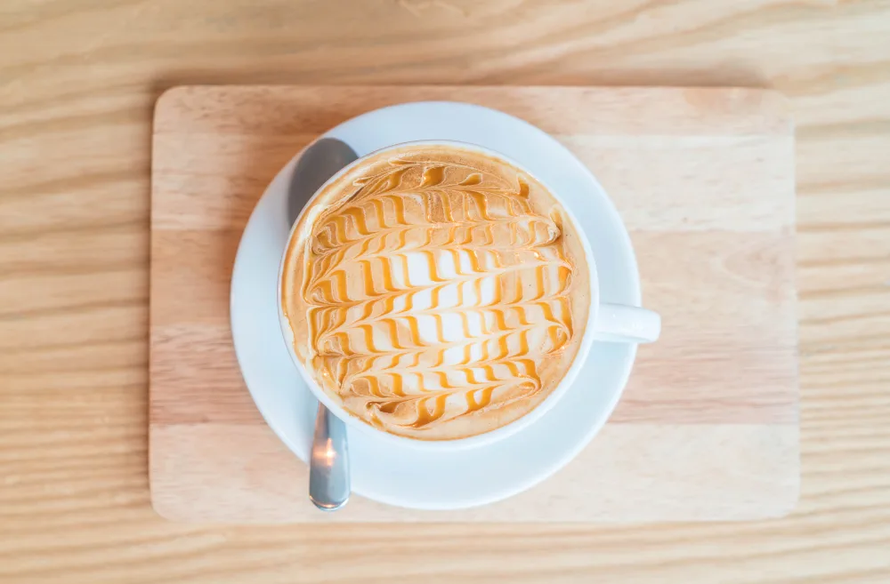 Cup of caramel latte with latte art on a wooden tray.