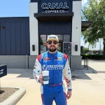 Race car driver holding a Canal Coffee Co. drink outside a coffee shop.