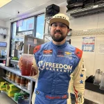 Race car driver holding a Canal Coffee Co. drink inside a coffee shop.